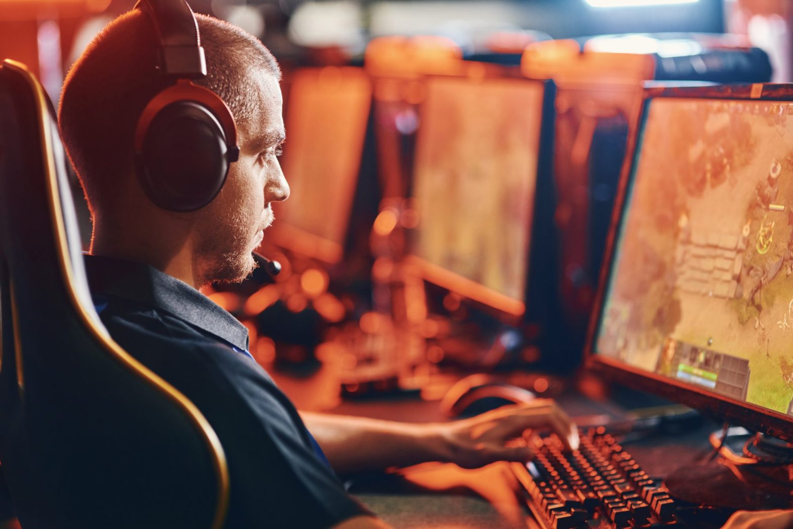 Privacy Policy In a dimly lit room filled with multiple screens, a man wearing headphones and a microphone is intensely focused on playing a computer game, training for the upcoming Corte Madera Esports Tournament.
