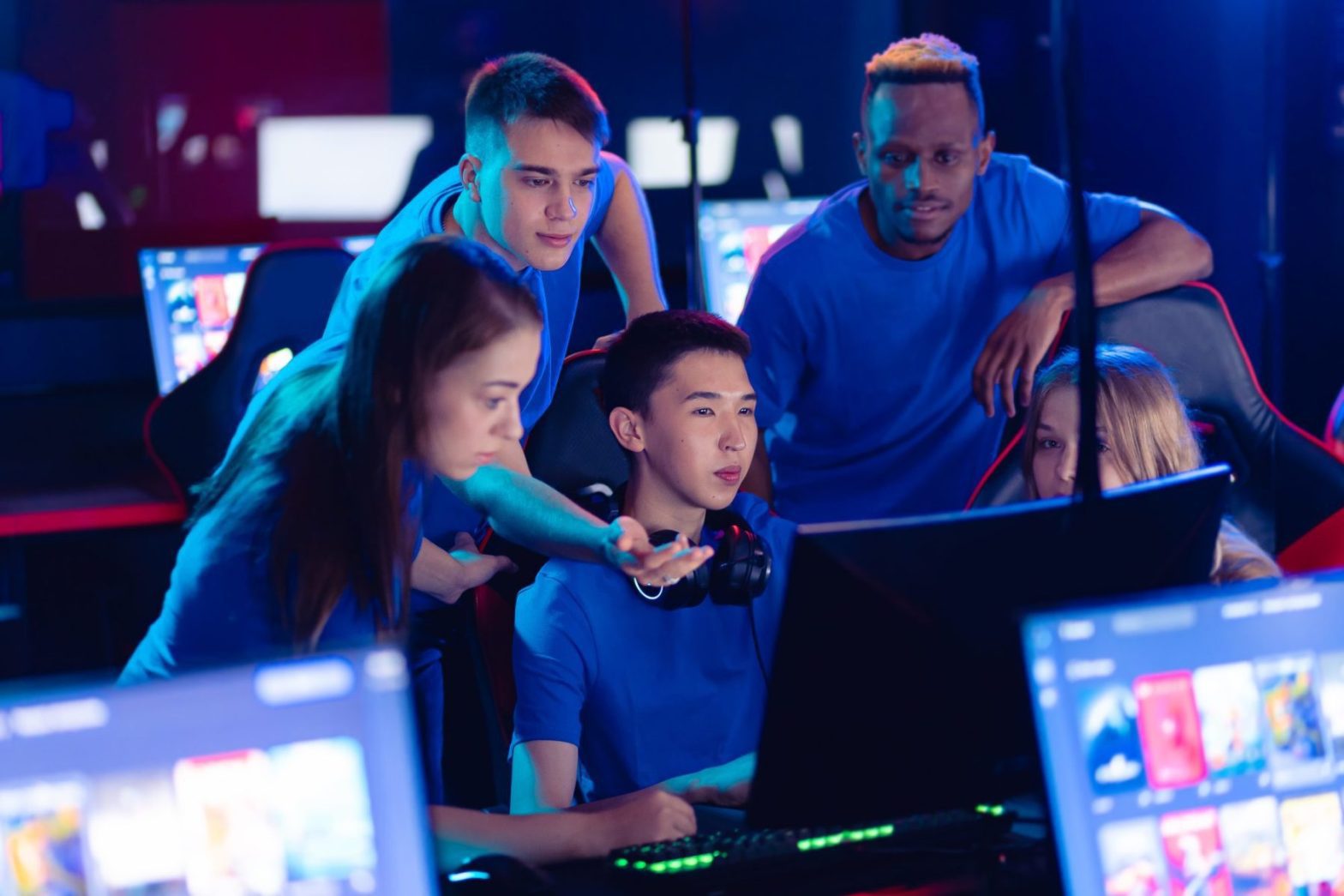 Accessibility Notifications In a dimly lit room, a group in blue shirts intently focuses on the computer monitor, strategizing for the San Rafael Esports event.