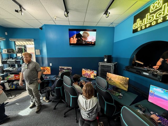 Kids and adults near gaming stations and wall screens at DubDub AI Arcade